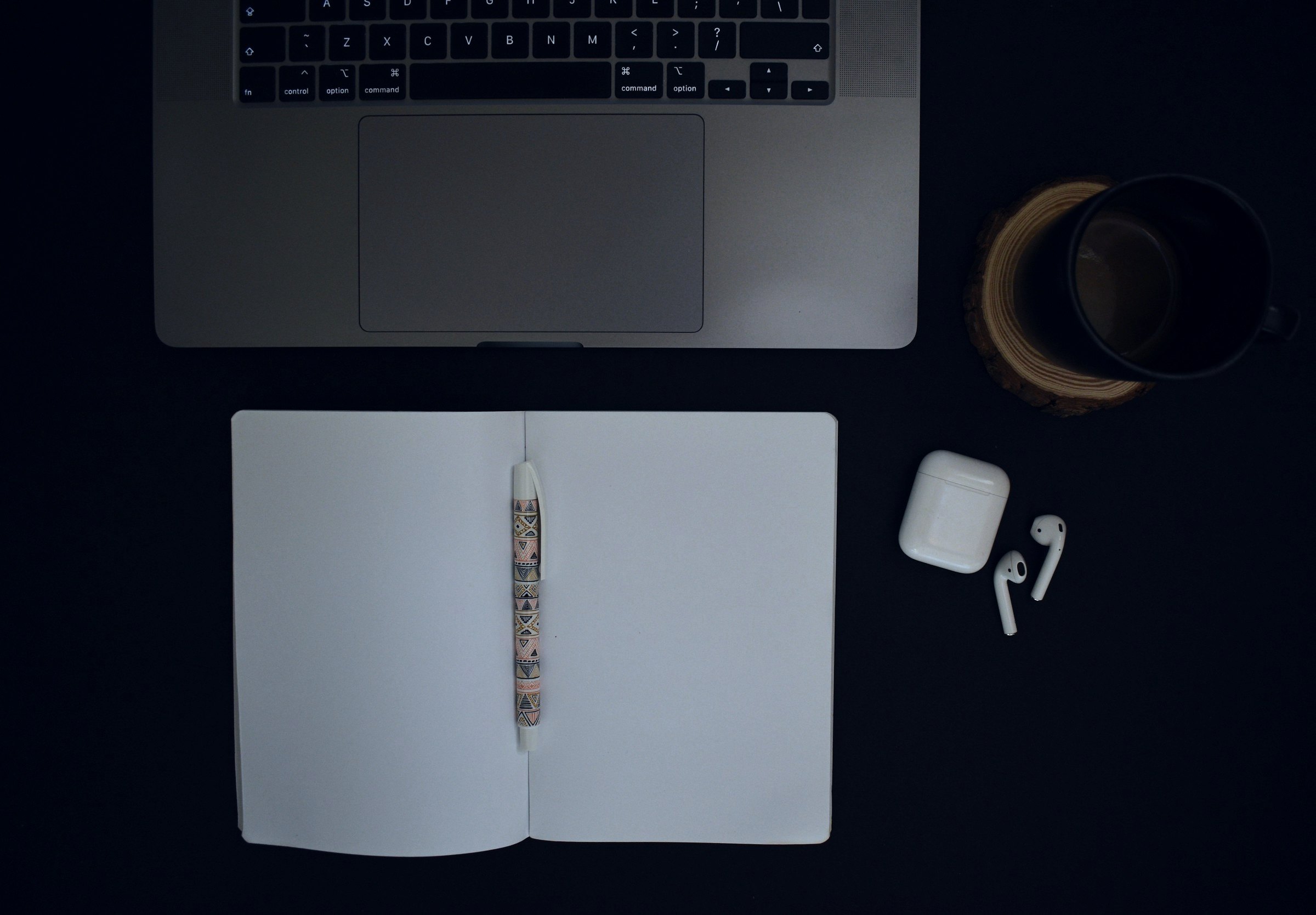 Notebook, pen and laptop on a dark desk